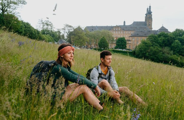 Diese Wanderer ruhen sich vor dem ehemaligen Benediktinerkloster Banz aus, einem der Highlights der Tourismusregion Obermain•Jura. | © Foto: djd/Tourismusregion Obermain•Jura/Jana Margarete Schuler